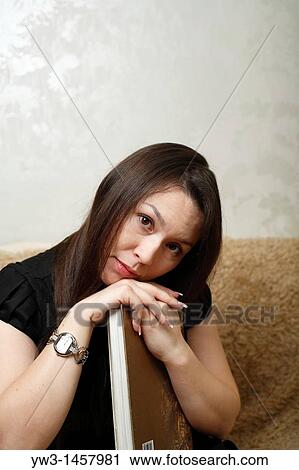 Stock Image - pretty brunette girl indoors on modern sofa. Fotosearch