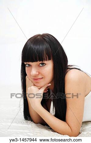 Picture - pretty brunette girl indoors on the bed smiling. Fotosearch