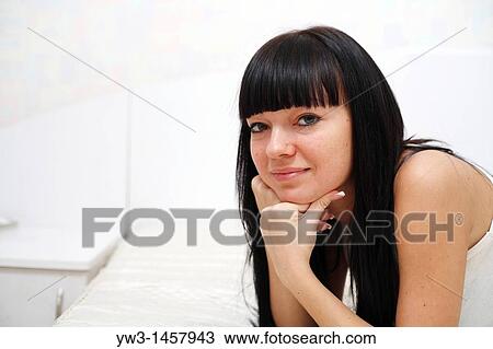 Stock Image - pretty brunette girl indoors on the bed smiling. Fotosearch