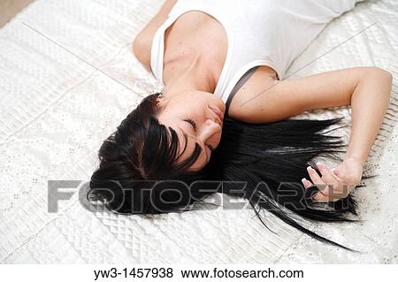 Stock Photo - pretty brunette girl lying on the bed indoors. Fotosearch