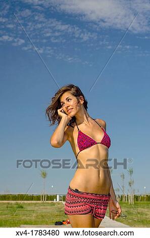 Stock Image - Pretty Brunette talk with mobile phone at Ebro riverside at ExpoZaragoza outdoors area, Saragossa, Aragon, Spain. Fotosearch