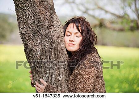 Stock Photography - Pretty brunette woman embracing tree. Fotosearch
