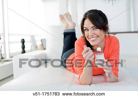Stock Image - Pretty brunette woman enjoying a yogurt at the sofa. Fotosearch