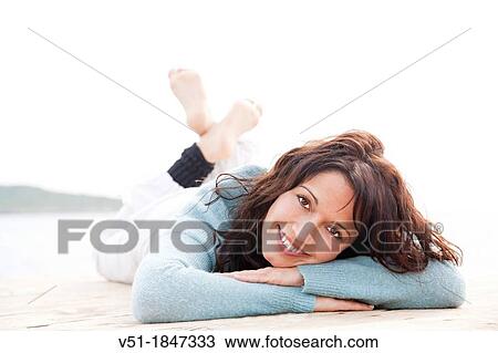 Stock Image - Pretty brunette woman lying on a seaside pier smiling at camera. Fotosearch