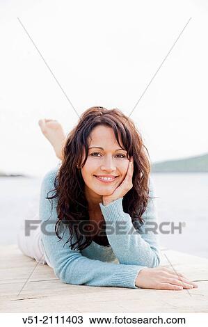 Pretty brunette woman lying on a seaside pier smiling at camera View Large Photo Image Stock Image - Pretty brunette woman lying on a seaside pier smiling at camera. Fotosearch
