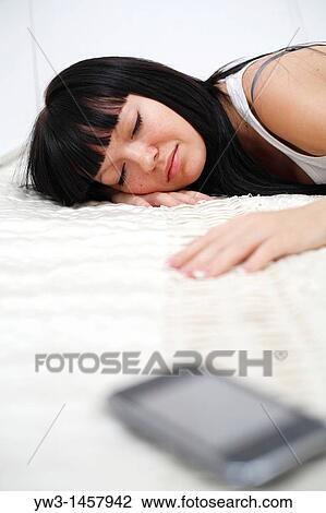 Stock Image - Pretty brunette woman sleeping on bed with cell phone. Fotosearch
