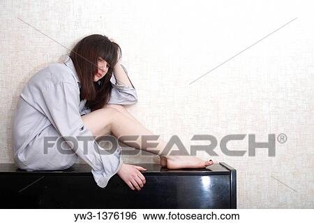 Stock Photograph - pretty brunette women indoors in shirt sitting on the top of piano. Fotosearch
