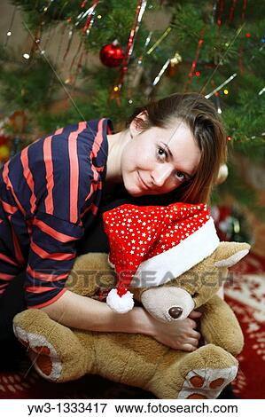 Stock Photo - pretty girl against decorated xmas tree with teddy bear. Fotosearch
