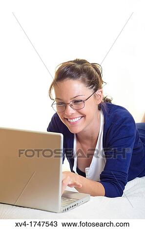 Stock Image - Pretty girl chatting on notebook in the bedroom. Fotosearch
