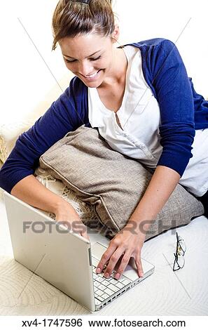 Stock Photograph - Pretty girl chatting on notebook in the bedroom. Fotosearch