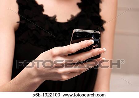 Stock Image - Pretty girl in little black dress texting on mobile phone. Fotosearch