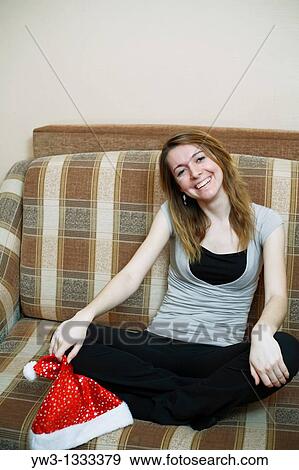 Stock Photo - pretty girl in the Christmas hat on sofa smiling. Fotosearch