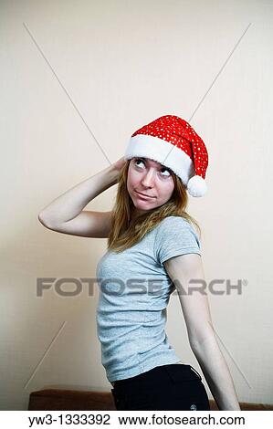 Stock Image - pretty girl in the Christmas hat against light wall posing. Fotosearch