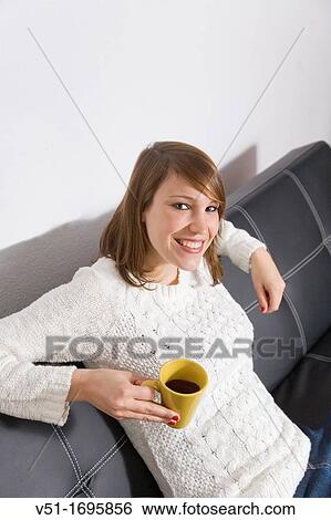 Pretty woman enjoying a coffe at home on the sofa, smiling at camera View Large Photo Image Stock Photograph - Pretty woman enjoying a coffe at home on the sofa, smiling at camera. Fotosearch