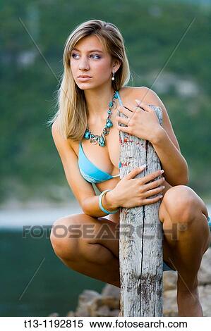 Pretty young woman in a swimsuit is posing besides a wooden pole View Large Photo Image Stock Photography - Pretty young woman in a swimsuit is posing besides a wooden pole. Fotosearch