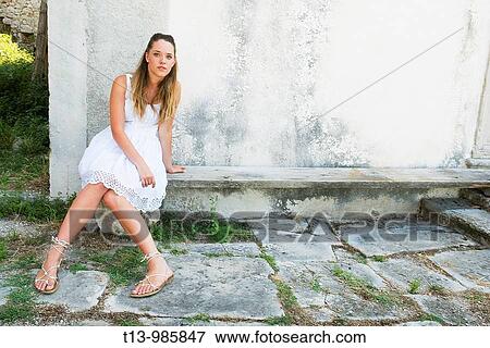 Stock Photo - Pretty young woman in White dress is sitting on wooden bench. Fotosearch