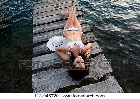Pretty young woman is lying on wooden pier in late afternoon View Large Photo Image Stock Image - Pretty young woman is lying on wooden pier in late afternoon. Fotosearch