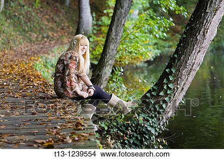 Pretty young woman is sitting in the park next to a peaceful lake View Large Photo Image Picture - Pretty young woman is sitting in the park next to a peaceful lake. Fotosearch