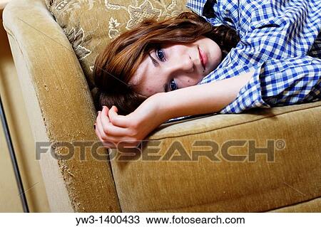 Stock Image - Pretty young woman lying on sofa, looking at camera. Fotosearch