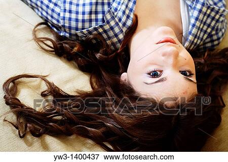Stock Photo - Pretty young woman lying on sofa, looking at camera. Fotosearch