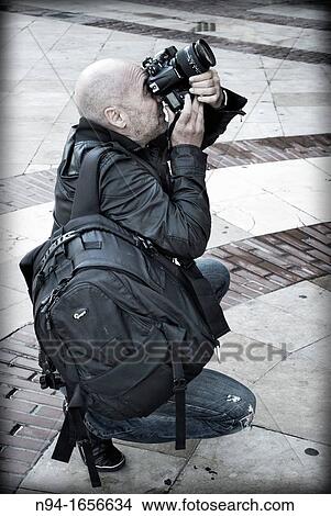 Picture - Professional Photographer backpacking, crouching and concentrate, taking photos with a digital SLR camera.. Fotosearch