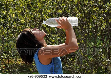 Stock Image - Profile of adolescent drinking some water fron plastic bottle in the park. Fotosearch