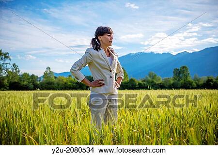 Picture - Proud woman standing up on a wheat field with mountain in background in ticino switzerland.. Fotosearch
