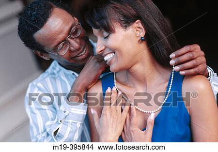 Picture - putting a necklace on his girlfriend/wife. Fotosearch