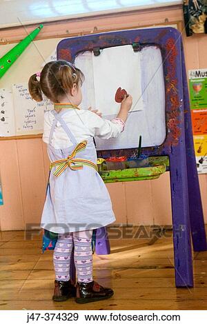 Rear view of a 3 year old girl, painting at nursrey school, with an apron on, concentrating. Standing at an easel View Large Photo Image Stock Photo - Rear view of a 3 year old girl, painting at nursrey school, with an apron on, concentrating. Standing at an easel. Fotosearch