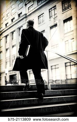 Rear view of a businessman climbing stairs unrecognizable on the street with a portfolio under his arm. City of London, England, UK, Europe. View Large Photo Image Stock Photo - Rear view of a businessman climbing stairs unrecognizable on the street with a portfolio under his arm. City of London, England, UK, Europe.. Fotosearch