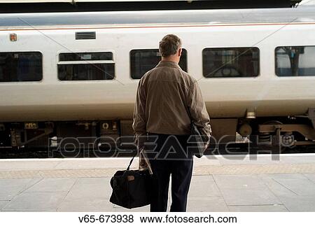 Rear view of a middle aged man holding a bag, waiting for train at Aberystwyth Railway station with Arriva wales train pulling into the station. Aberystwyth Wales UK View Large Photo Image Stock Photo - Rear view of a middle aged man holding a bag, waiting for train at Aberystwyth Railway station with Arriva wales train pulling into the station. Aberystwyth Wales UK. Fotosearch