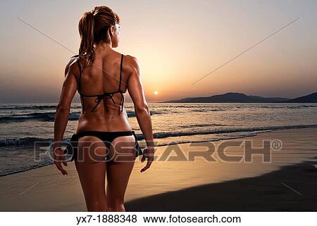 Stock Photo - Rear view of a woman in bikini at the beach at sunset. Tarifa, Costa de la Luz, Cadiz, Andalusia, Spain, Europe.. Fotosearch