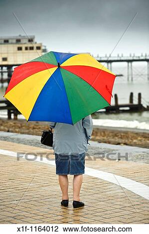 Rear view of a woman sheltering under an umbrella on Aberystwyth promenade in the rain july wet summer afternoon, Wales UK View Large Photo Image Stock Image - Rear view of a woman sheltering under an umbrella on Aberystwyth promenade in the rain july wet summer afternoon, Wales UK. Fotosearch
