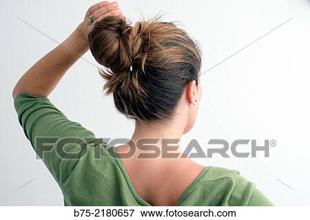 Stock Photo - Rear view of a young blond hair woman with a bun on the head and raised arm and hand in her hair.. Fotosearch