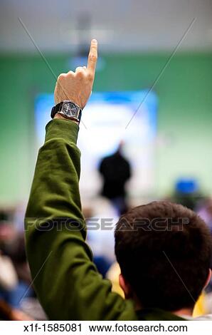 Rear view of a young man holding his hand up to ask a question in a meeting, UK View Large Photo Image Stock Image - Rear view of a young man holding his hand up to ask a question in a meeting, UK. Fotosearch