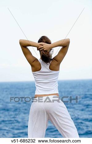 Rear view of a young woman standing by the sea View Large Photo Image Stock Image - Rear view of a young woman standing by the sea. Fotosearch