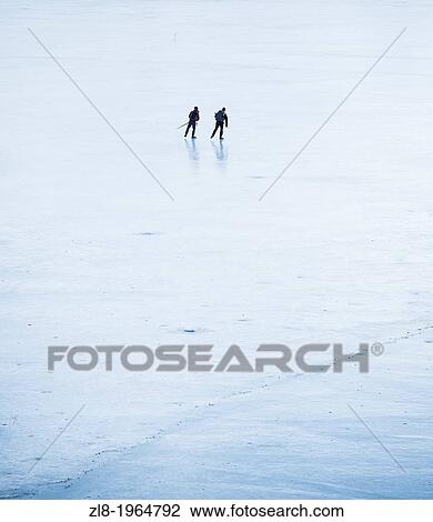 Stock Image - Rear view of two men iceskating with touring skates on lake. Stockholm, Sweden.. Fotosearch