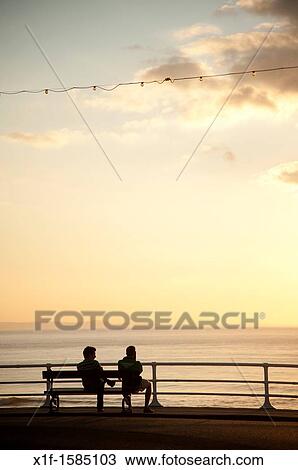 rear view of two men sitting on a bench at sundown, looking out to sea, aberystwyth wales uk View Large Photo Image Stock Image - rear view of two men sitting on a bench at sundown, looking out to sea, aberystwyth wales uk. Fotosearch