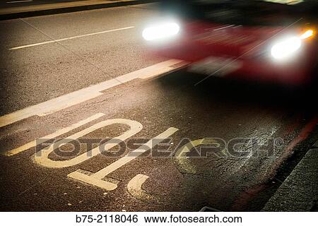 Red car with lights circulating at night by a road with a Stop painted on the asphalt. London, England, UK, Europe. View Large Photo Image Stock Photograph - Red car with lights circulating at night by a road with a Stop painted on the asphalt. London, England, UK, Europe.. Fotosearch