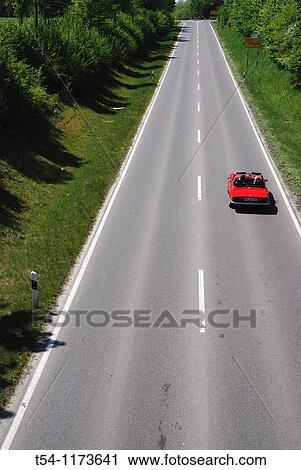 Stock Image - Red convertible on a country road in Bavaria. Fotosearch
