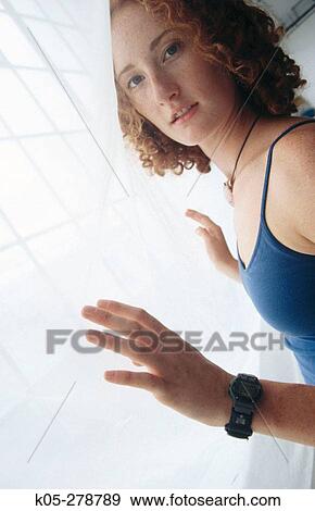Stock Photo - Red haired girl leaning with hands against curtain. Fotosearch