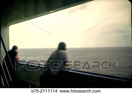 Reflection in a window of a passenger boat of two men leaning on the railing of the deck overlooking the sea. View Large Photo Image Picture - Reflection in a window of a passenger boat of two men leaning on the railing of the deck overlooking the sea.. Fotosearch