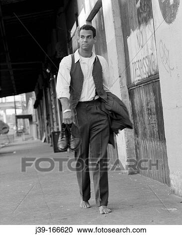 Stock Image - Relaxed businessman walking, holding shoes. Fotosearch
