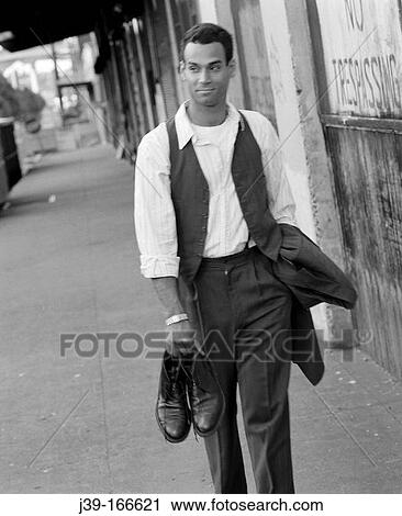 Stock Image - Relaxed businessman walking, holding shoes. Fotosearch