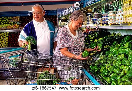Stock Photo - Retired senior couple shopping for groceries and vegetables together in grocery store looking for healthy foods. Fotosearch