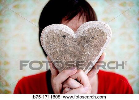 Stock Photo - Retrato de mujer de pelo moreno con corazon tapando la cara, amor, Portrait of brown-haired woman covering her face with heart, love. Fotosearch