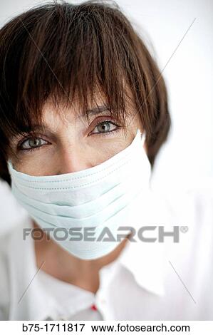 Stock Photo - Retrato de mujer de pelo moreno, ojos verdes y mascarilla tapando la boca, Portrait of brown-haired woman, green eyes and a mask covering the mouth. Fotosearch