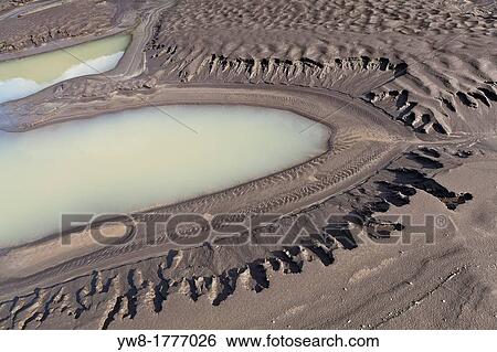Stock Photograph - River bed, and mud flats with ash from volcanic eruptions, Virkisjokull Glacier on Vatnajokull Ice Cap, Iceland. Fotosearch