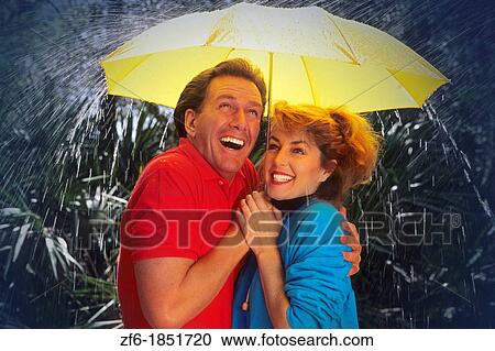 Romantic fun couple huddled together under an umbrella during a short spring shower View Large Photo Image Stock Image - Romantic fun couple huddled together under an umbrella during a short spring shower. Fotosearch