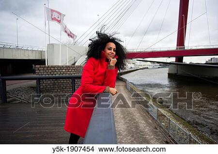 Rotterdam, Netherlands. Young, African woman with a red winter coat, pondering and looking out over the river, next to the Willemsbrug in Rotterdam. View Large Photo Image Picture - Rotterdam, Netherlands. Young, African woman with a red winter coat, pondering and looking out over the river, next to the Willemsbrug in Rotterdam.. Fotosearch